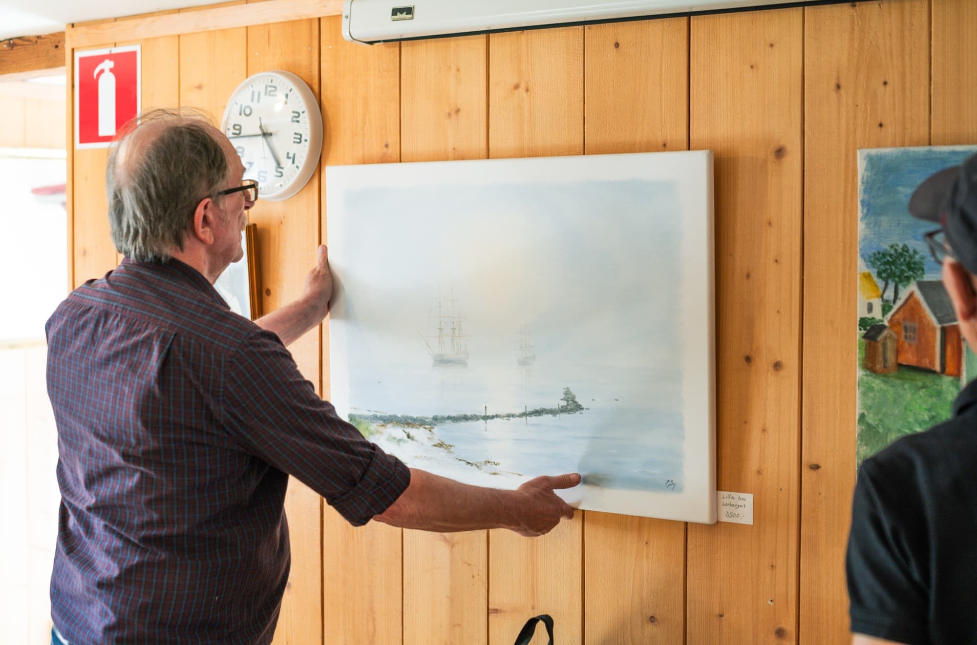 Ingvar Stendahl hänger upp en av sina dimmiga havsmålningar på en trävägg under en utställning.