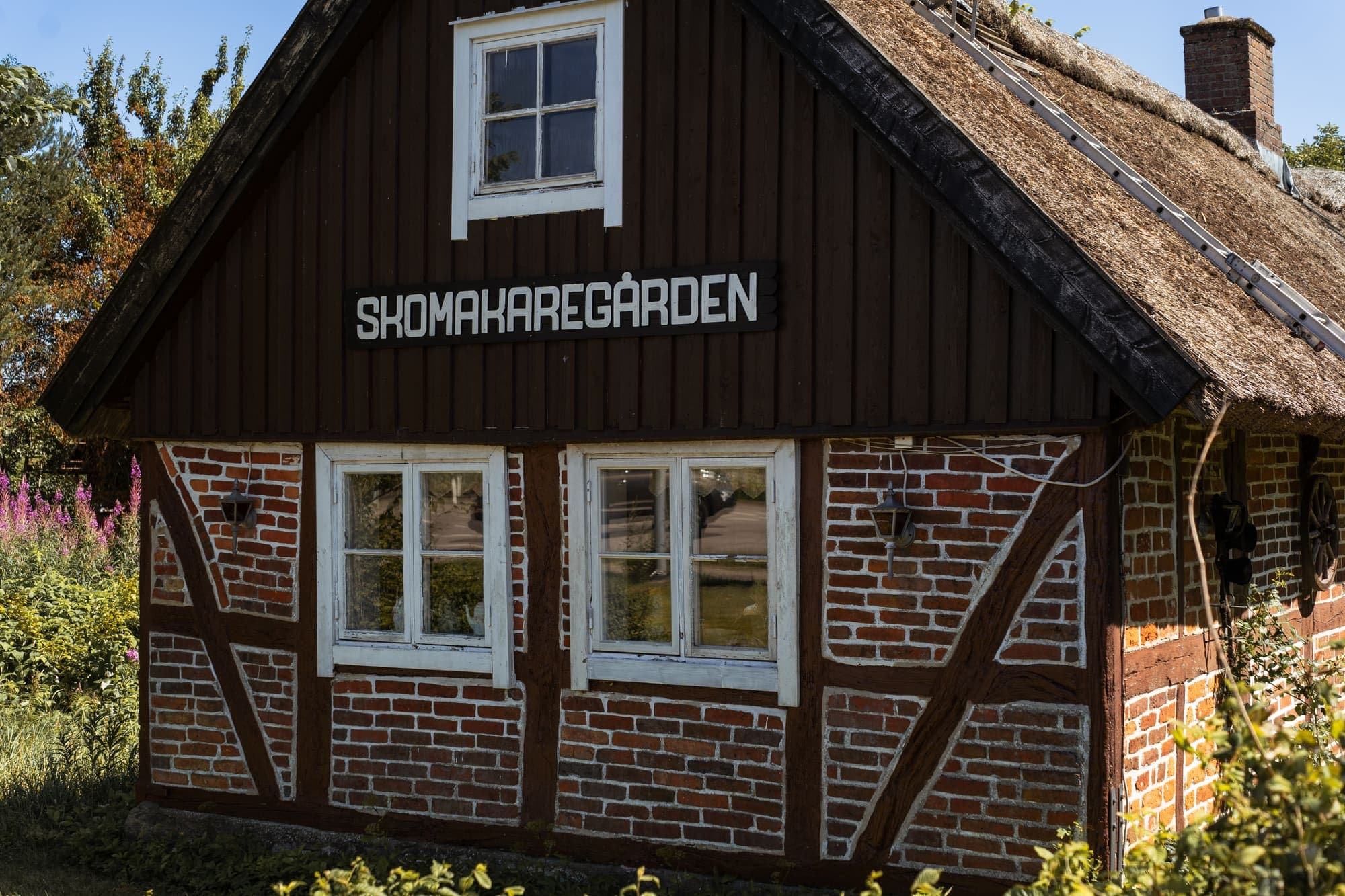 Skomakaregården, ett korsvirkeshus med halmtak och skylt med gårdens namn på gaveln.