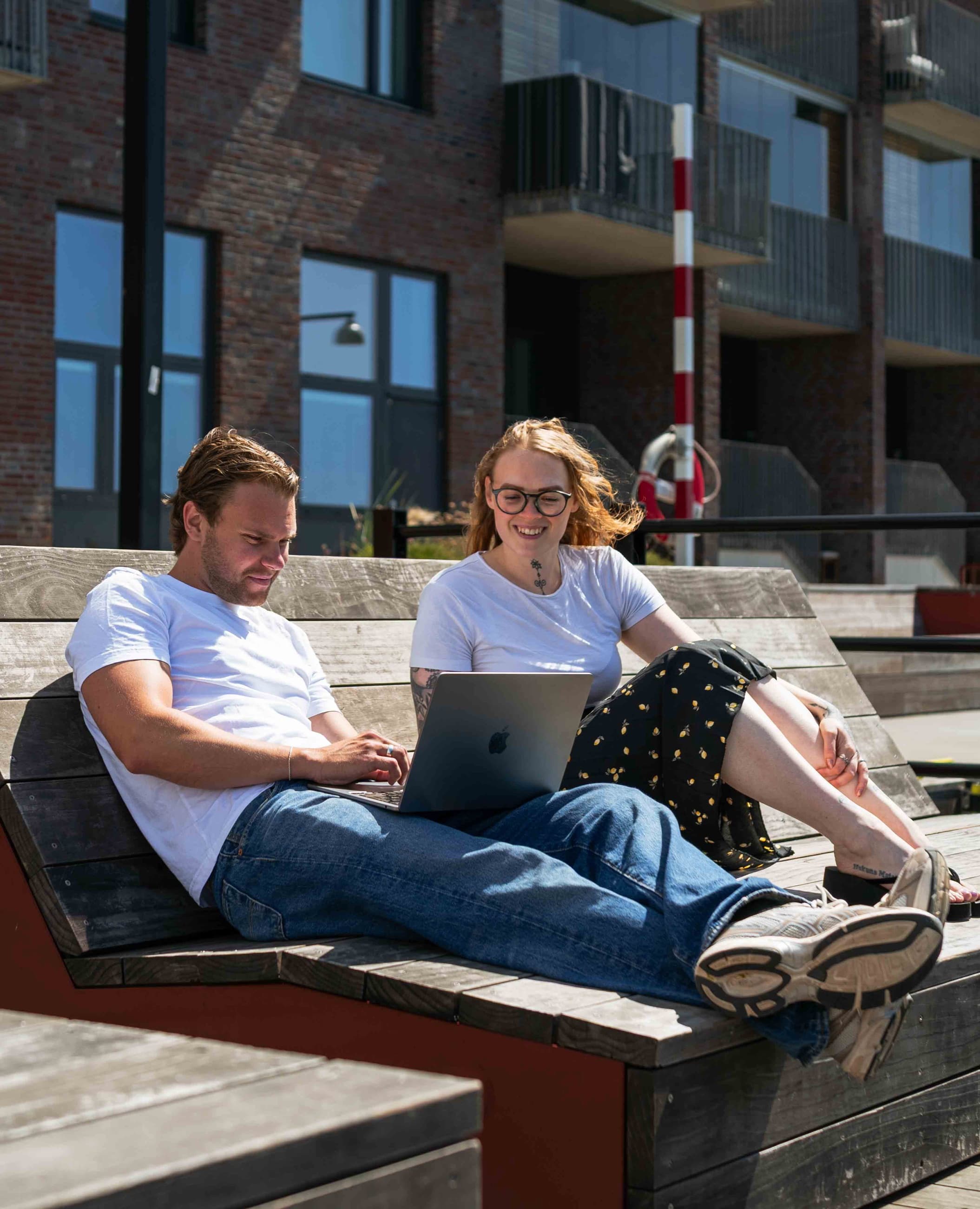 Två personer sitter vid en bank och tittar på en laptop. Äkta foto kontra arkivbild