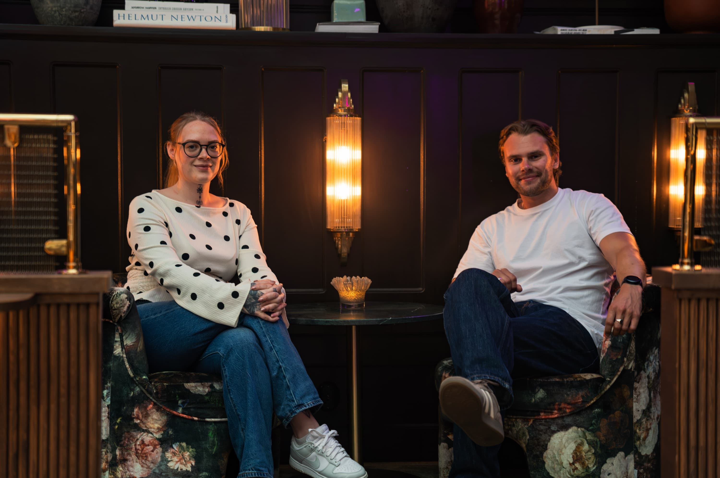 Mikaela och Theo sitter i varsin blommig fåtölj i en varmt upplyst art nouveau-lounge i Malmö.